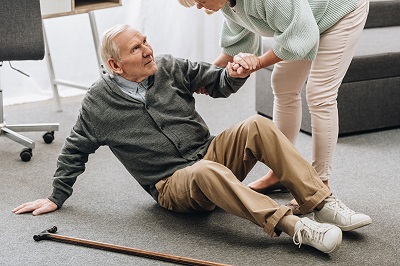 picture of an elderly man who has had a fall being assisted to stand back up