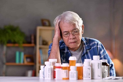 picture of an elderly lady sitting in front of many pills (Polypharmacy)